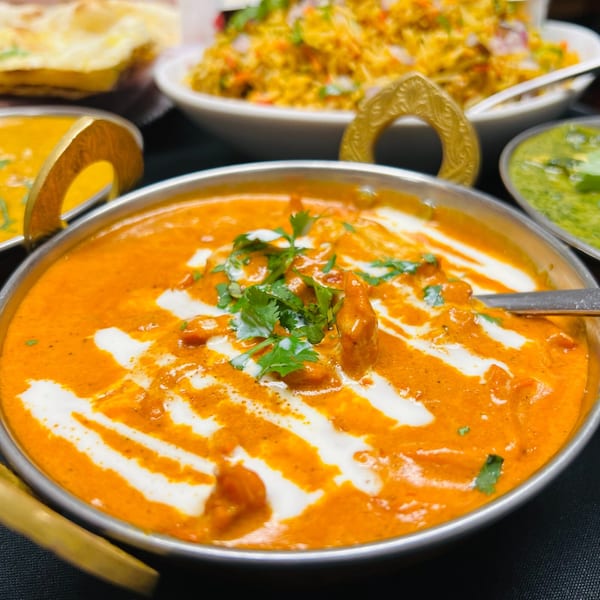 Close-up of creamy orange Indian butter chicken in a silver bowl, garnished with cilantro and cream swirls.