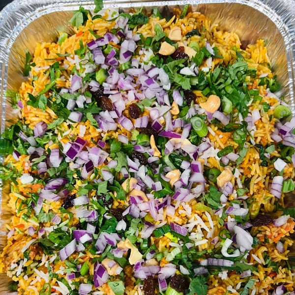 Close-up of Indian biryani in a foil tray, topped with red onions, cilantro, and cashews.