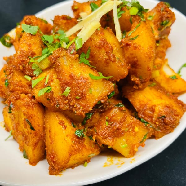Spicy Indian potato dish, Aloo Tikki, garnished with fresh cilantro and ginger slivers.
