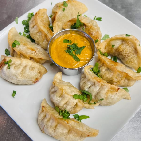 Fried Indian momos, garnished with cilantro, surrounding a small bowl of orange dipping sauce.