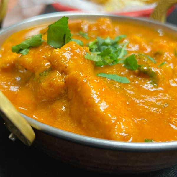 Close-up of vibrant orange Indian curry with chicken and fresh cilantro in a metal bowl.