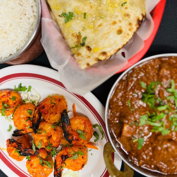 Overhead view of Indian food: shrimp skewers, rice, naan, and a bowl of curry.
