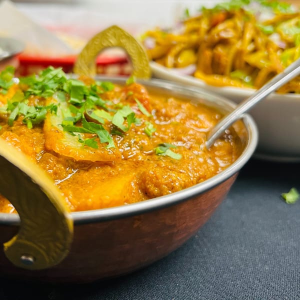 Close-up of a copper bowl filled with Indian curry, garnished with fresh cilantro.