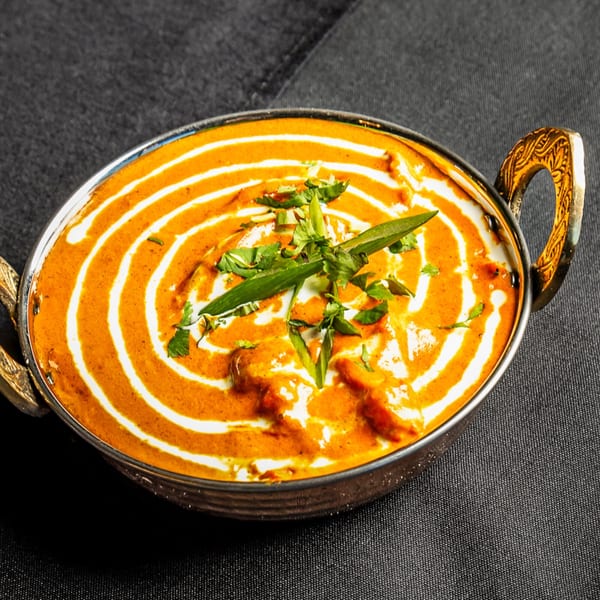 Indian butter chicken curry, garnished with cream swirls and fresh herbs, in a traditional metal bowl.