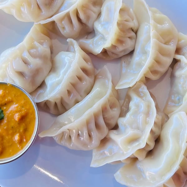 A plate of steamed momos, traditional Indian dumplings, with a side of orange dipping sauce.