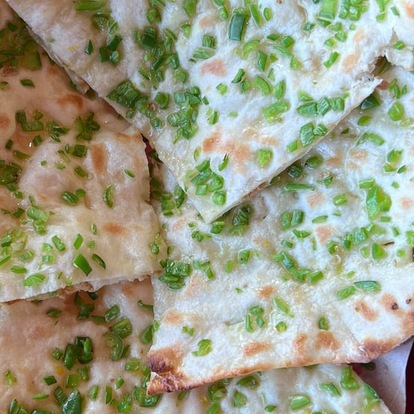 Close-up of several pieces of garlic naan from India Express Denver, topped with chopped green onions.