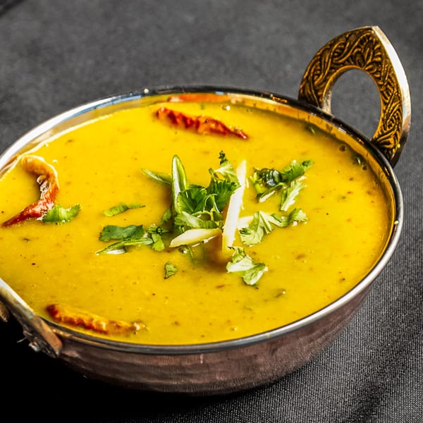 Golden yellow Indian dal in a decorative metal bowl, garnished with cilantro and red chilies.