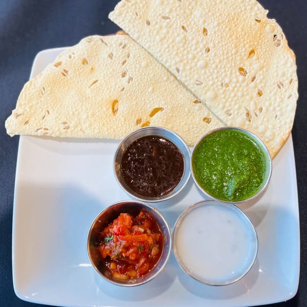 Crispy Indian papadum flatbreads with four small bowls of colorful chutneys and sauces.