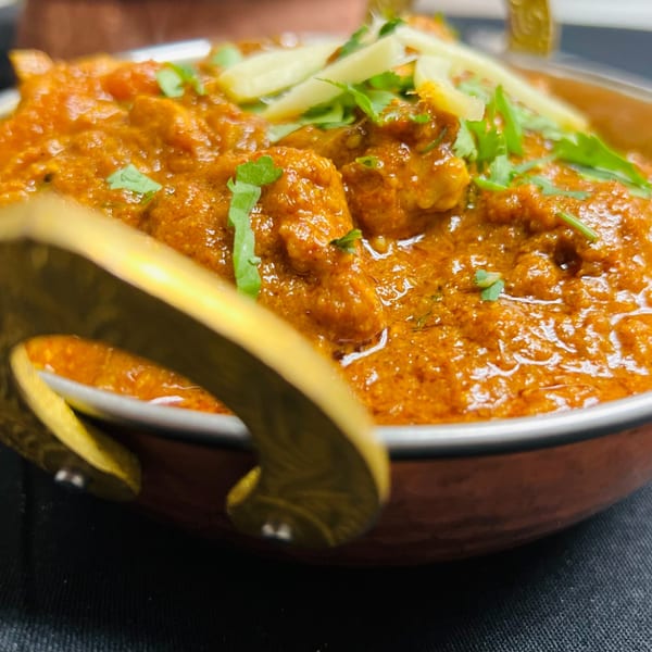 Close-up of India Express Denver's chicken curry, garnished with cilantro and ginger, in a copper bowl.