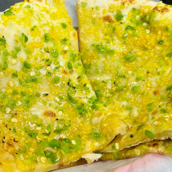 Close-up of two pieces of Indian Express Denver's chili naan, topped with green chilies and spices.