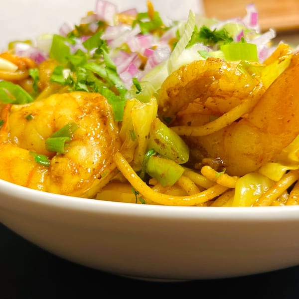 Close-up of Indian Express Denver's shrimp noodles with onions, cabbage, and green herbs.