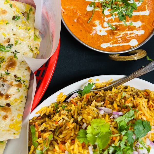 Indian food spread with naan bread, butter chicken, and biryani rice on a black background.