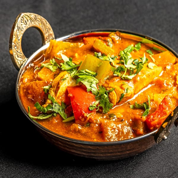 Indian Express Denver's chicken curry with bell peppers and cilantro in a decorative metal bowl.