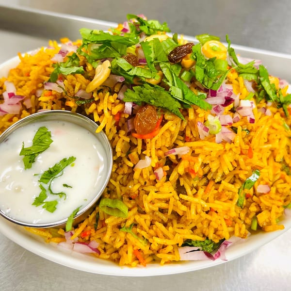 A large serving of Indian biryani rice with cashews, raisins, cilantro, and red onions, with a side of raita.