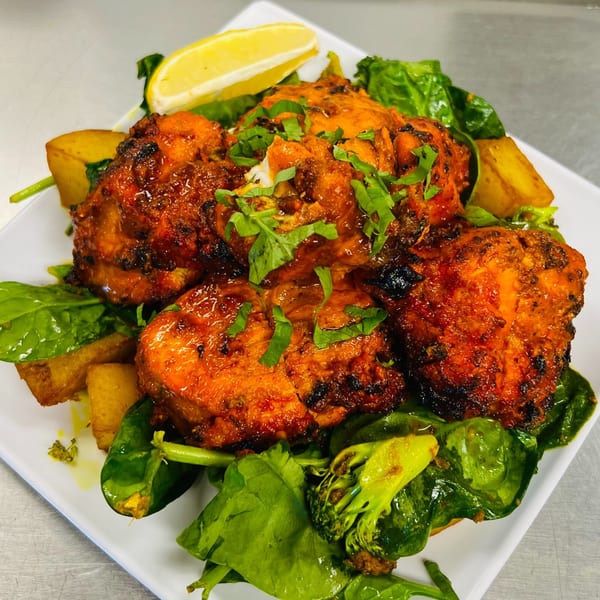 Indian Express Denver's Tandoori Chicken, garnished with cilantro, lemon, spinach, and roasted potatoes.