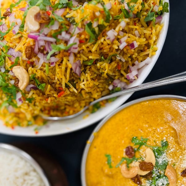 Close-up of Indian Express Denver's biryani with cashews, raisins, and red onion, alongside a bowl of curry.