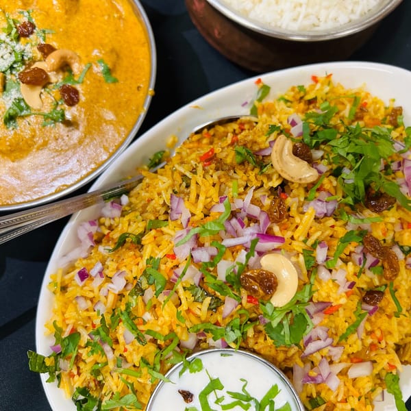 Close-up of Indian Express Denver's biryani with cashews, raisins, red onions, and cilantro, alongside curry.