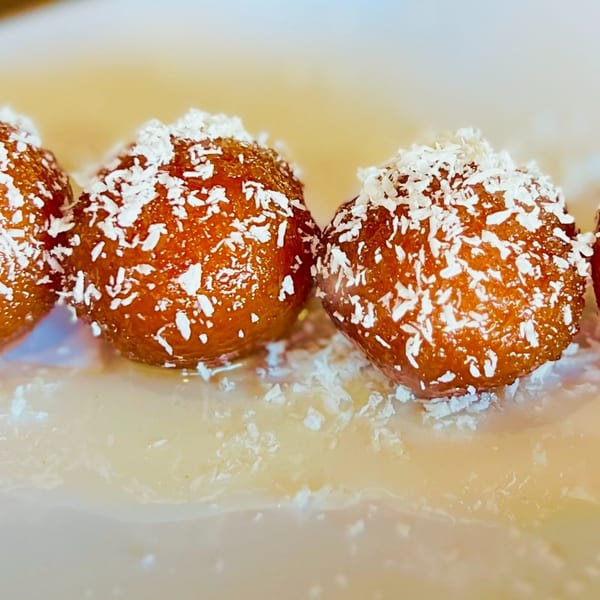 Close-up of three gulab jamun, Indian fried dough balls, topped with shredded coconut and syrup.