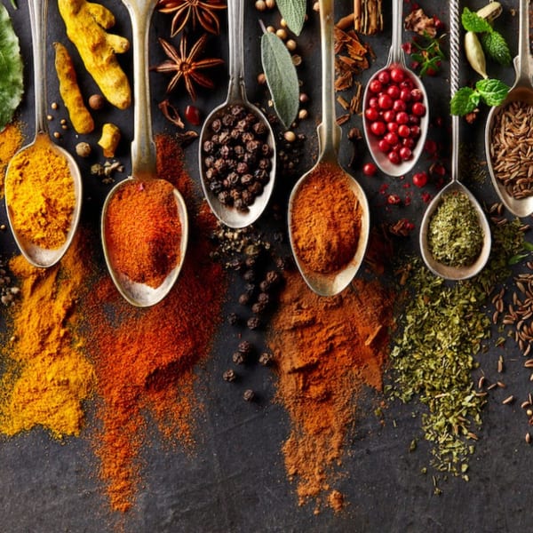 Assortment of vibrant Indian spices in spoons and scattered on a dark surface.