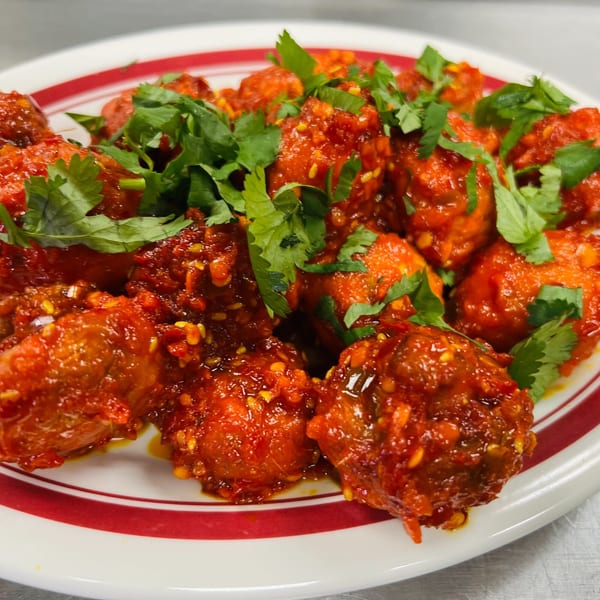 Close-up of vibrant red Indian Express chicken Manchurian, garnished with fresh green cilantro on a white plate.
